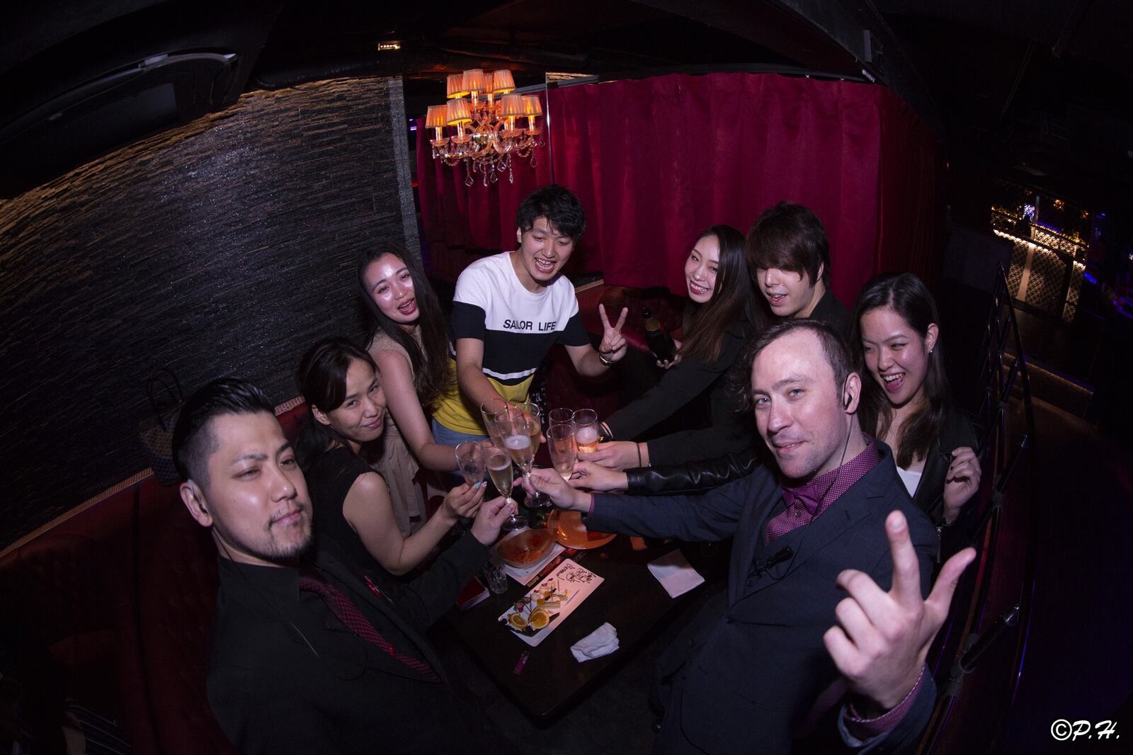 Renaud and a group raising their glasses in a lounge with red curtains