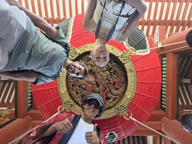 Guests looking up beneath the carved base of a red lantern in Asakusa