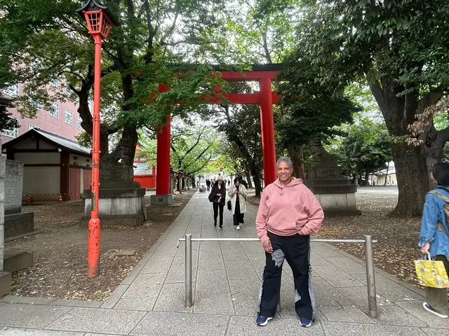 Guest standing beneath a red torii on a leafy shrine path