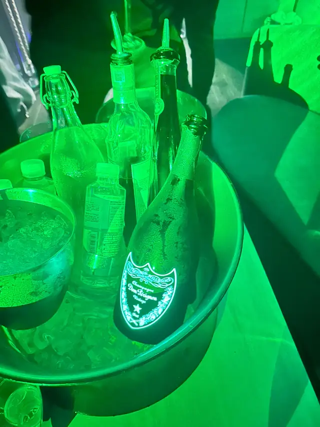 Champagne and other bottles beside an ice bucket under green club lighting