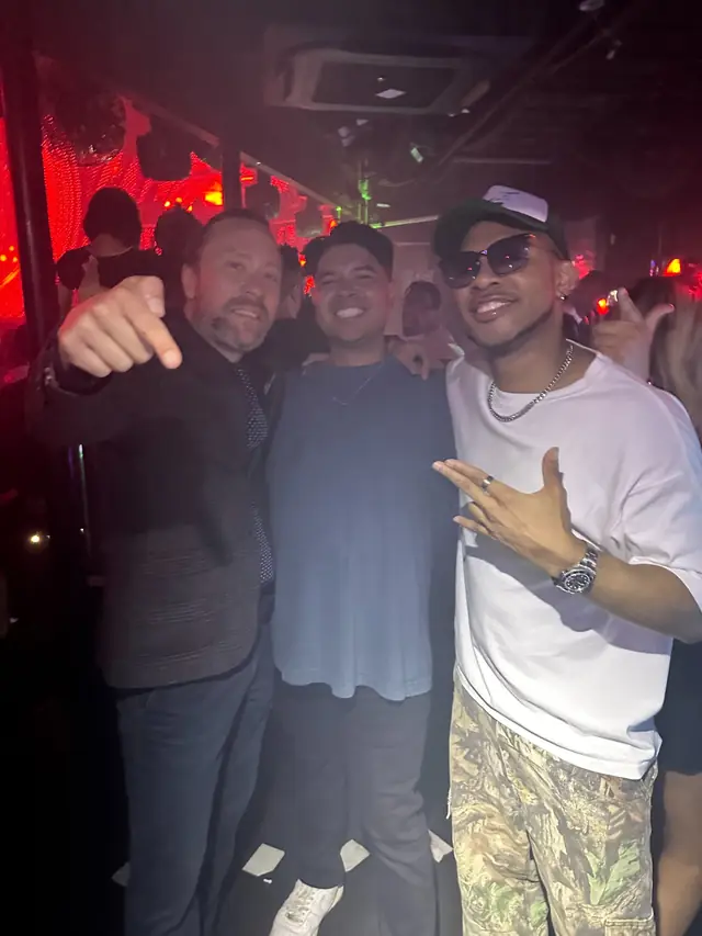 Three men posing together in a club with red lighting