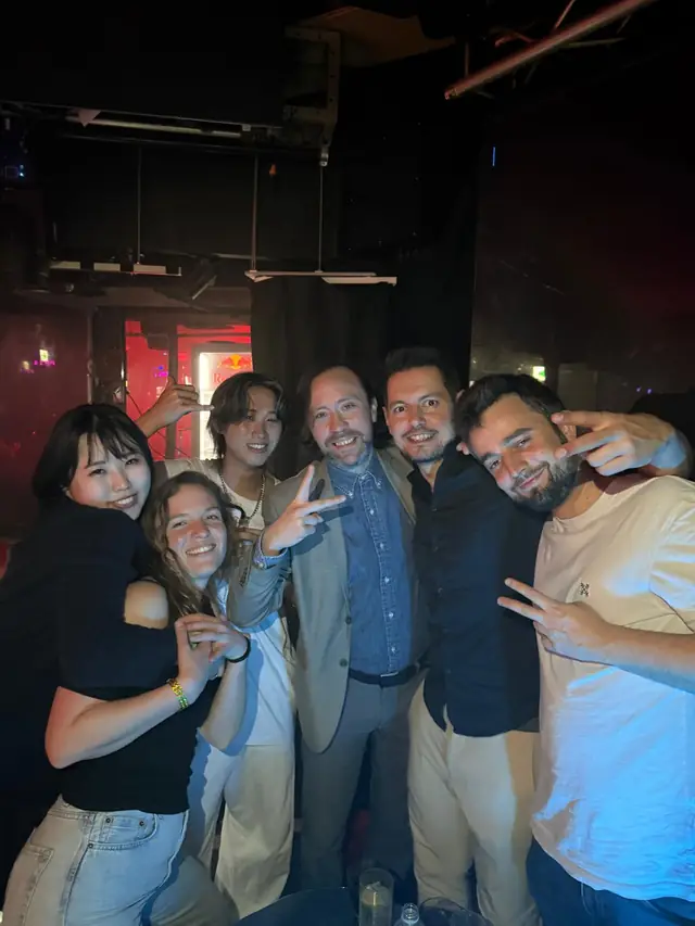 Six people smiling and posing together in a dimly lit club interior