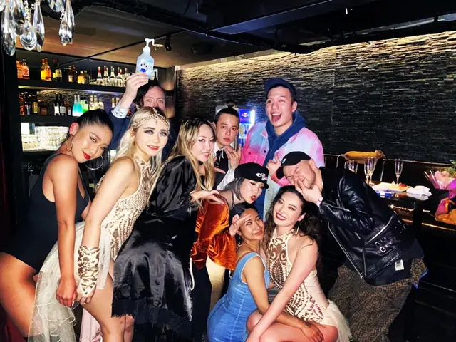 Group posing together in a bar, with bottles on shelves and glasses in the background.