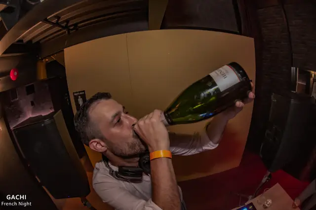A man with headphones around his neck drinking from a champagne bottle during a party