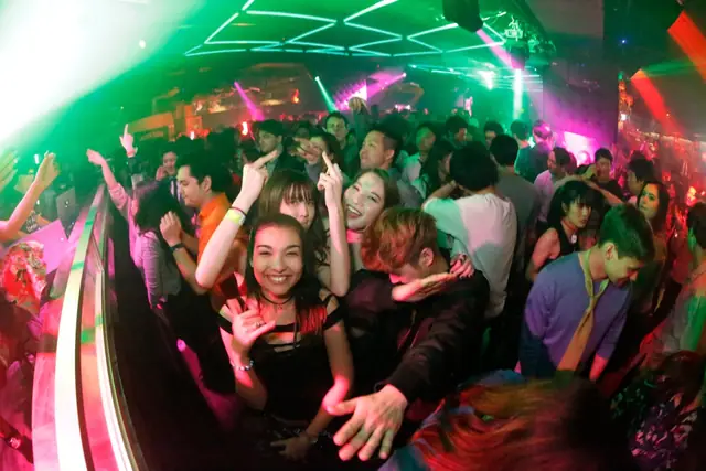 People dancing and posing on a crowded dance floor under green and pink club lights.