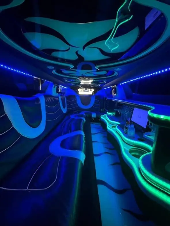 Blue and green lighting inside a limousine, with curved seating and a drinks counter.