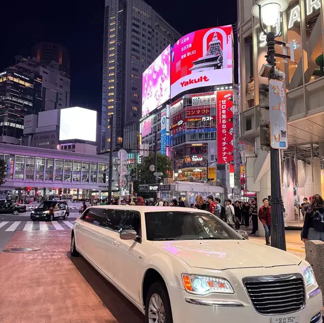 A white stretch limousine on a busy street beneath illuminated billboards at night.
