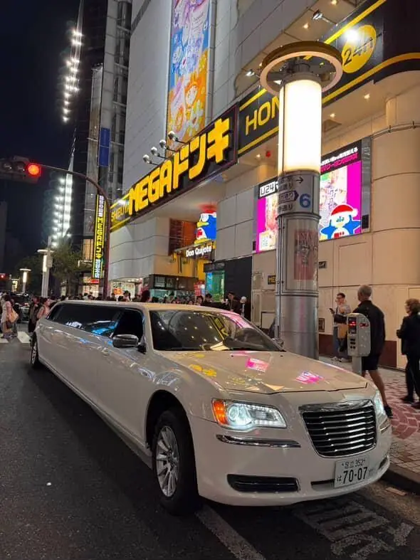 A white stretch limousine parked outside MEGA Don Quijote at night.