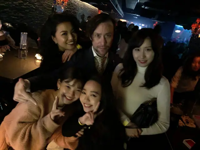 Five people posing together in a dimly lit lounge with a busy club in the background.
