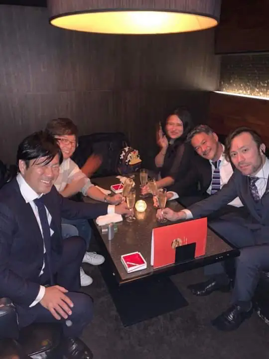 Five people seated around a lounge table, with several glasses raised for a toast.