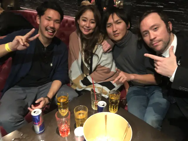 Four people seated together on a red sofa behind a table with drinks and an ice bucket.