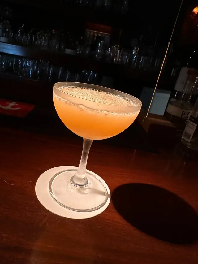 An orange-coloured cocktail in a stemmed glass on a wooden bar counter